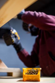 Focused construction worker drilling into wood, yellow box of screws in foreground.