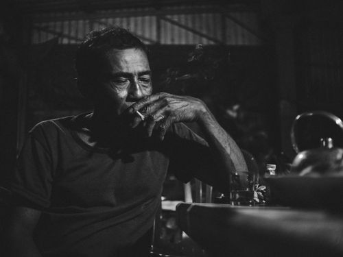 Free A contemplative man smokes quietly indoors, captured in dramatic black and white tones. Stock Photo