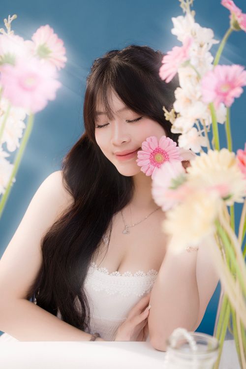 Free A young woman enjoying tranquility among pastel flowers in a serene indoor setting. Stock Photo