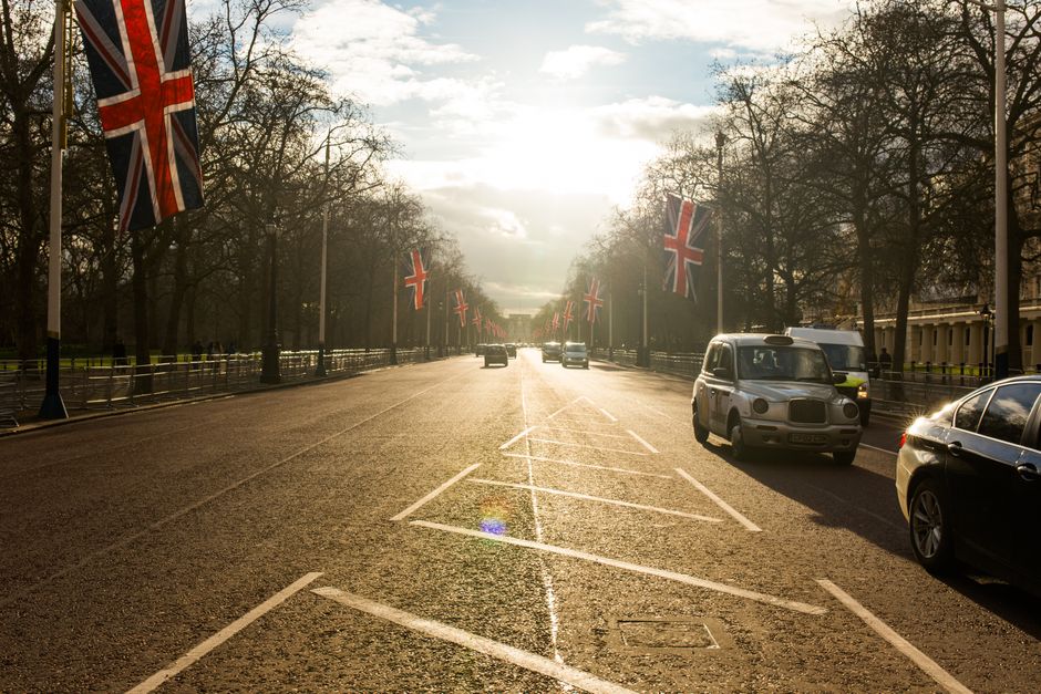 A scenic view of a road lined with Union Jack flags and cars in London.