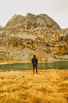 A person stands by a lake, gazing at the majestic mountains during fall in Saint-Martin-Vésubie, France.