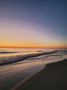 Tranquil sunrise on a beach with soft waves and vibrant sky.