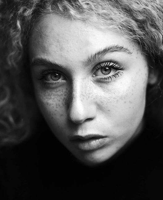 Black and white portrait of a freckled woman with captivating eyes, set in a classic style.