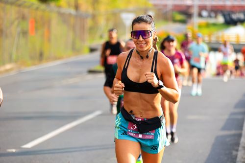 Free Fit female athlete running in a marathon during a sunny day, smiling with determination. Stock Photo