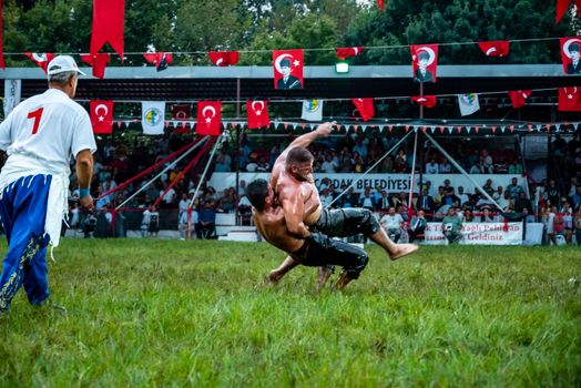 Exciting oil wrestling match with spectators and Turkish flags on display.