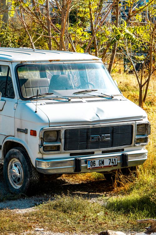 Free A classic white GMC van parked amidst lush greenery under bright sunshine. Stock Photo