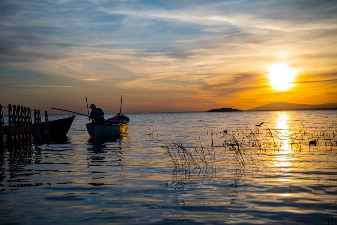 Serene Sunset Over Lake with Fisherman in Boat · Free Stock Photo