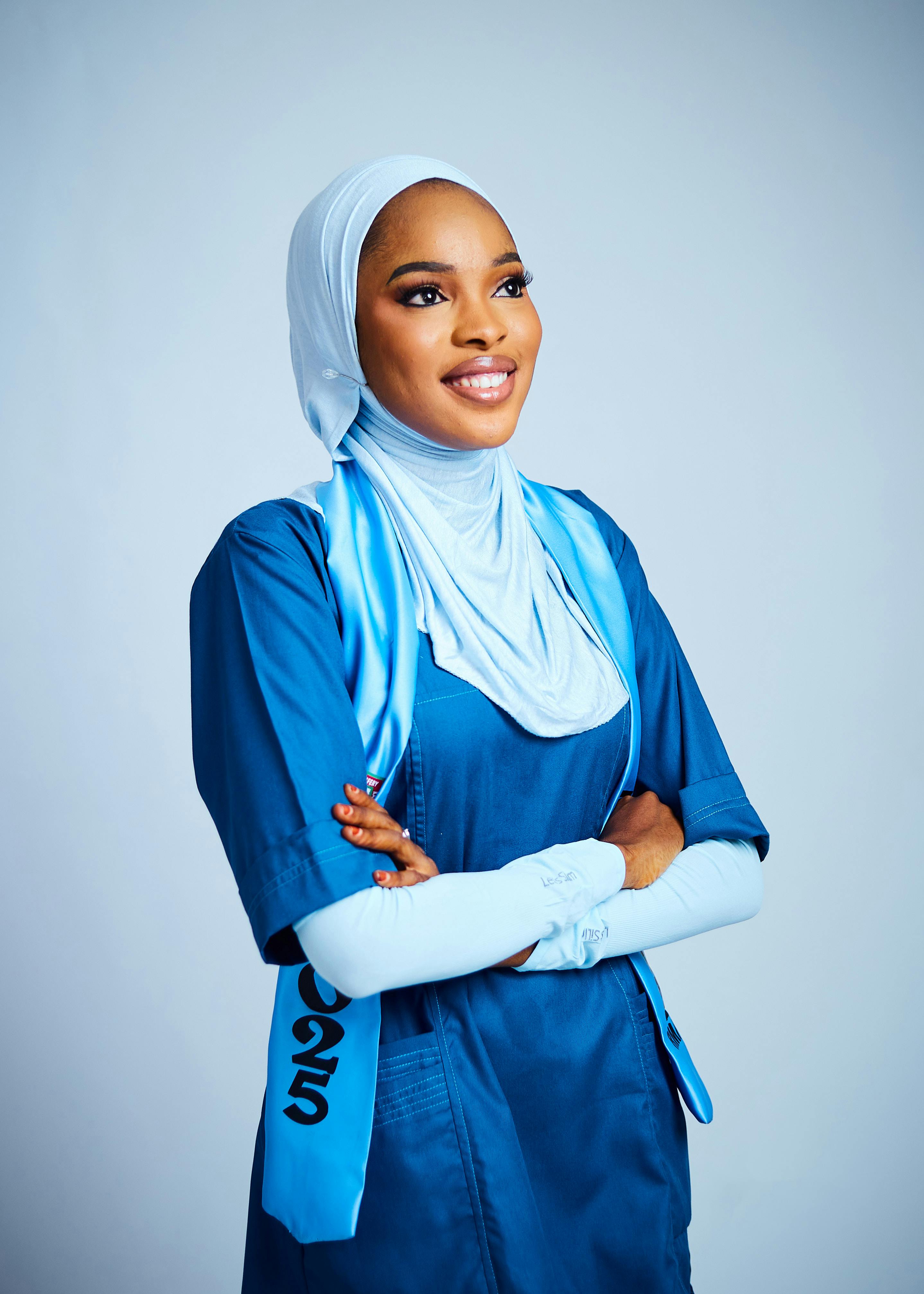Smiling female nurse in blue uniform with folded arms, exuding confidence and professionalism.
