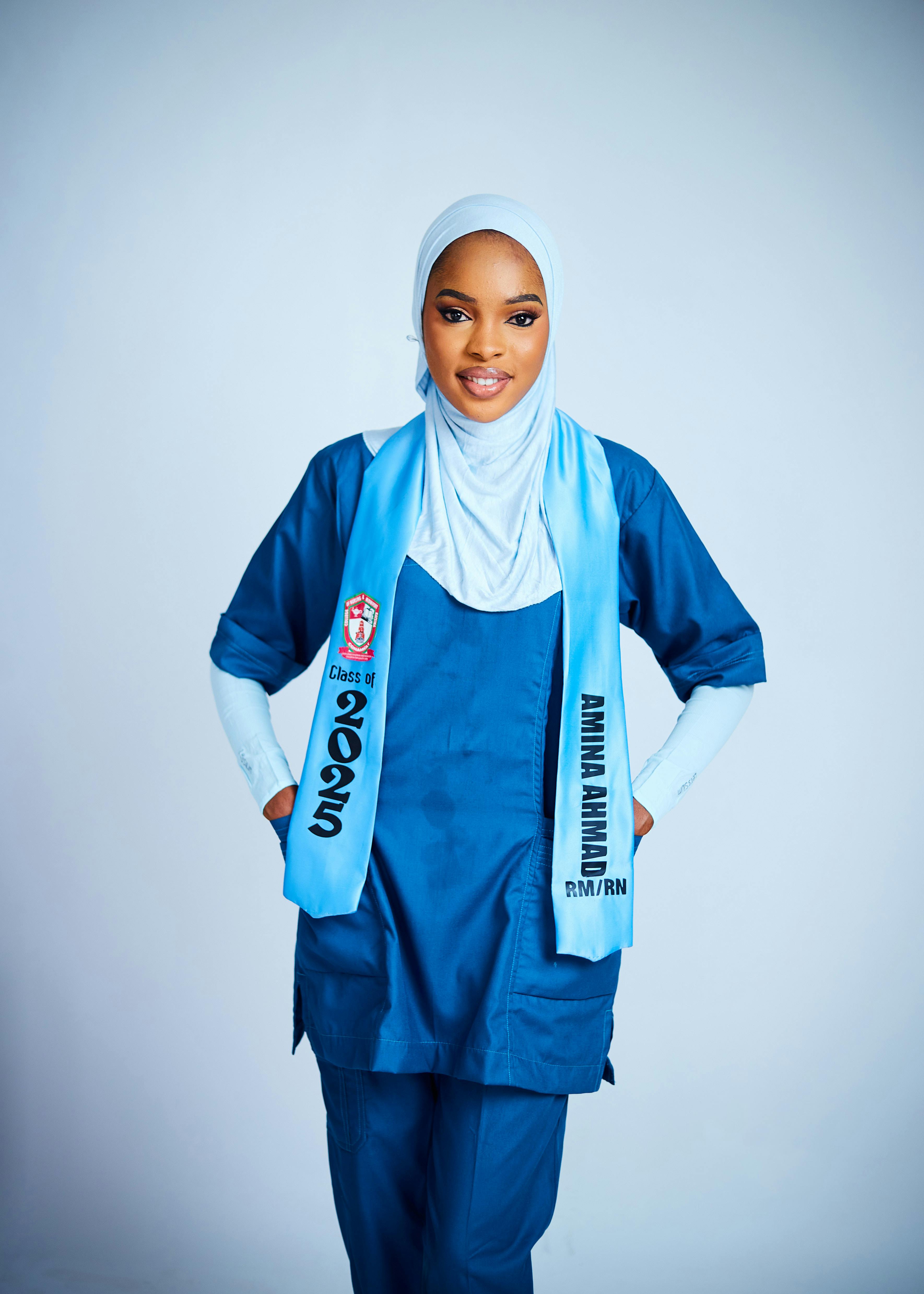 Young woman wearing hijab and graduation sash, posing proudly indoors.