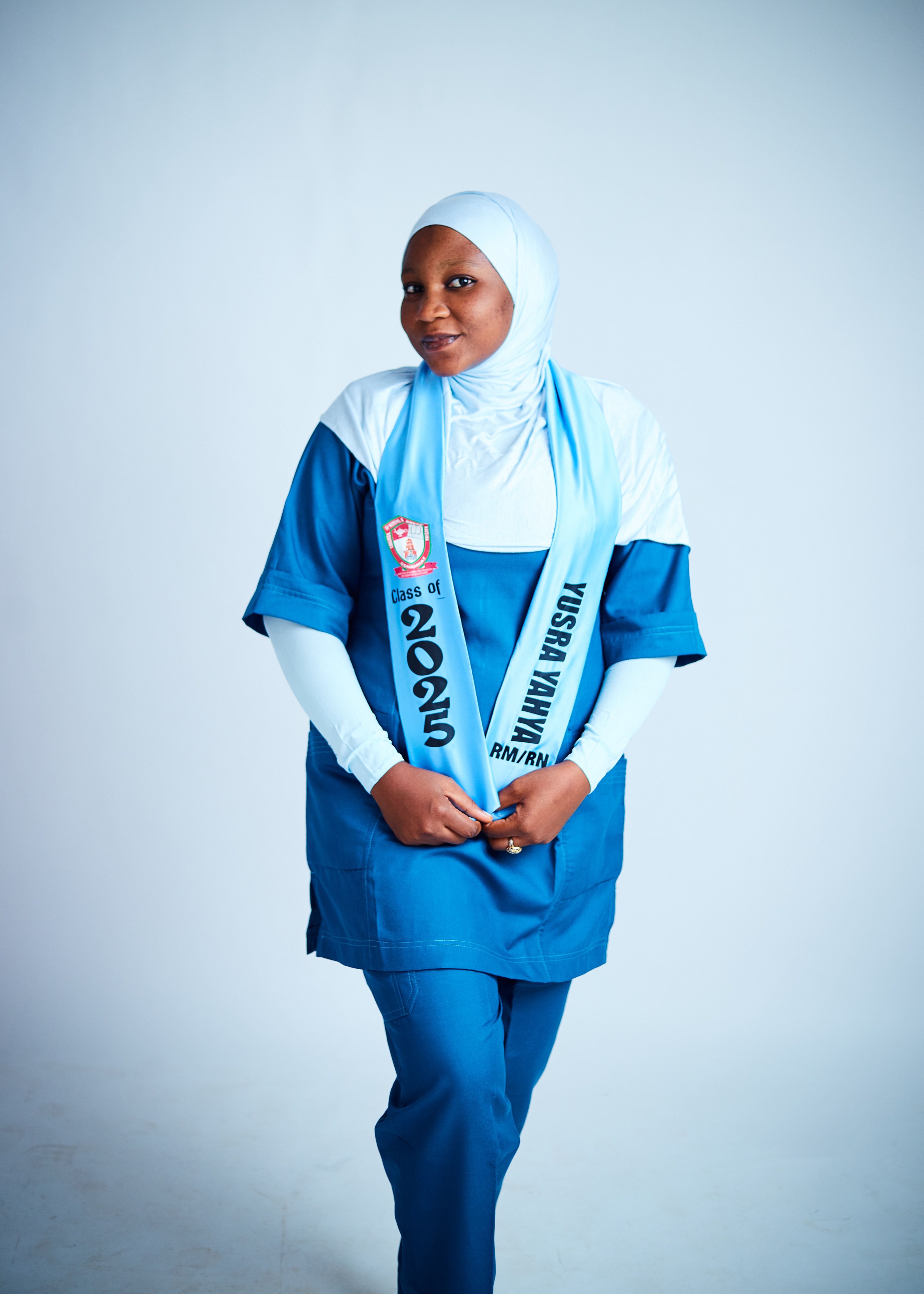 Young female graduate in blue uniform with a Class of 2023 sash against light background.