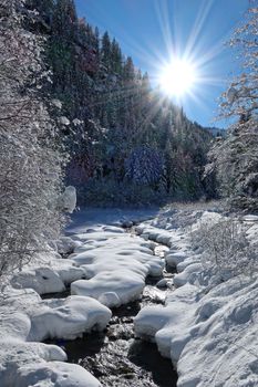 Breathtaking snowy river scene in Chamonix-Mont-Blanc with sunlit forest.