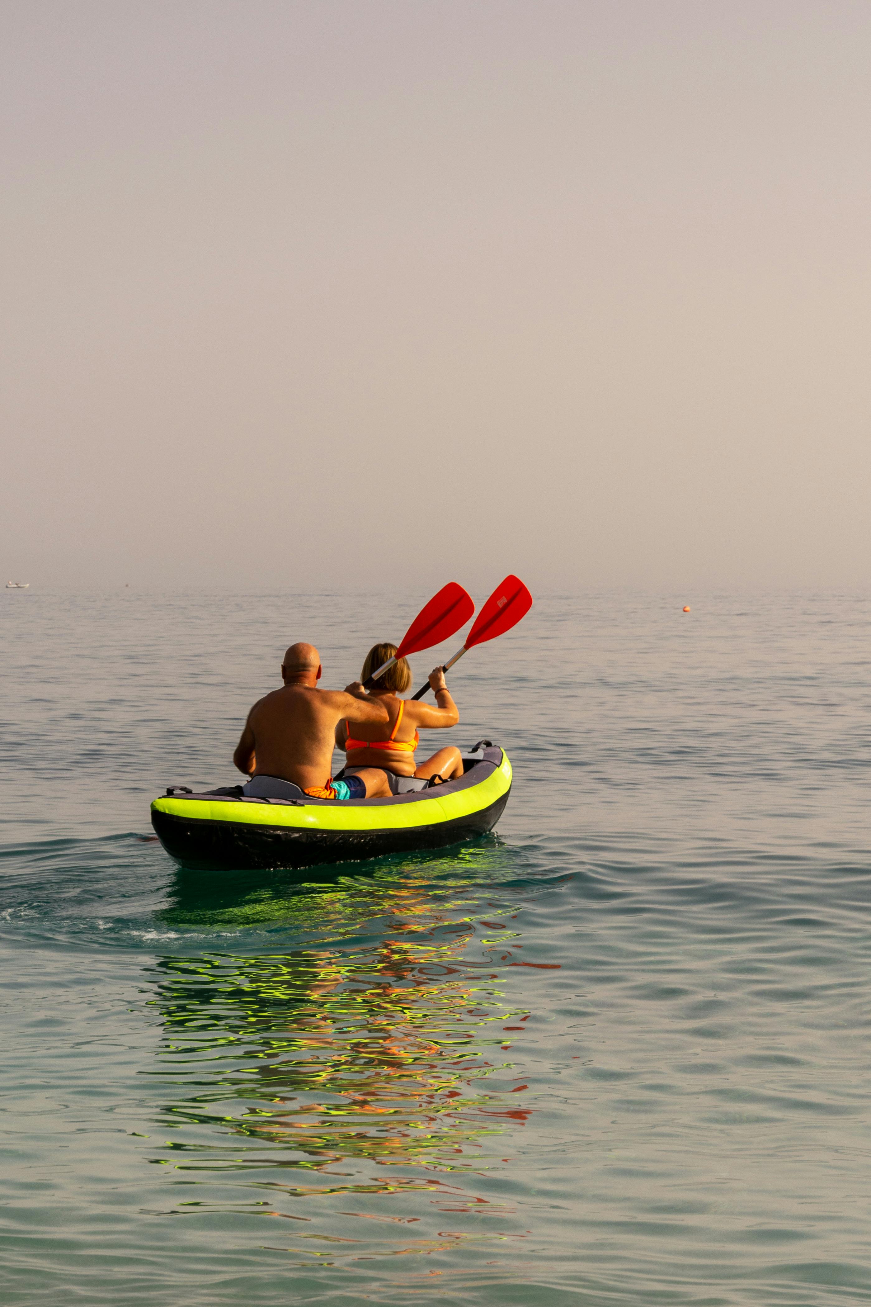 A couple kayaking on a tranquil ocean during a clear summer day.