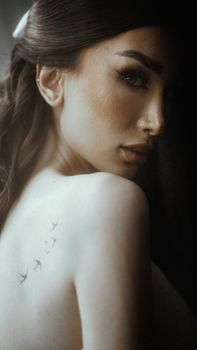 A mysterious portrait capturing a woman with bird tattoo on her shoulder