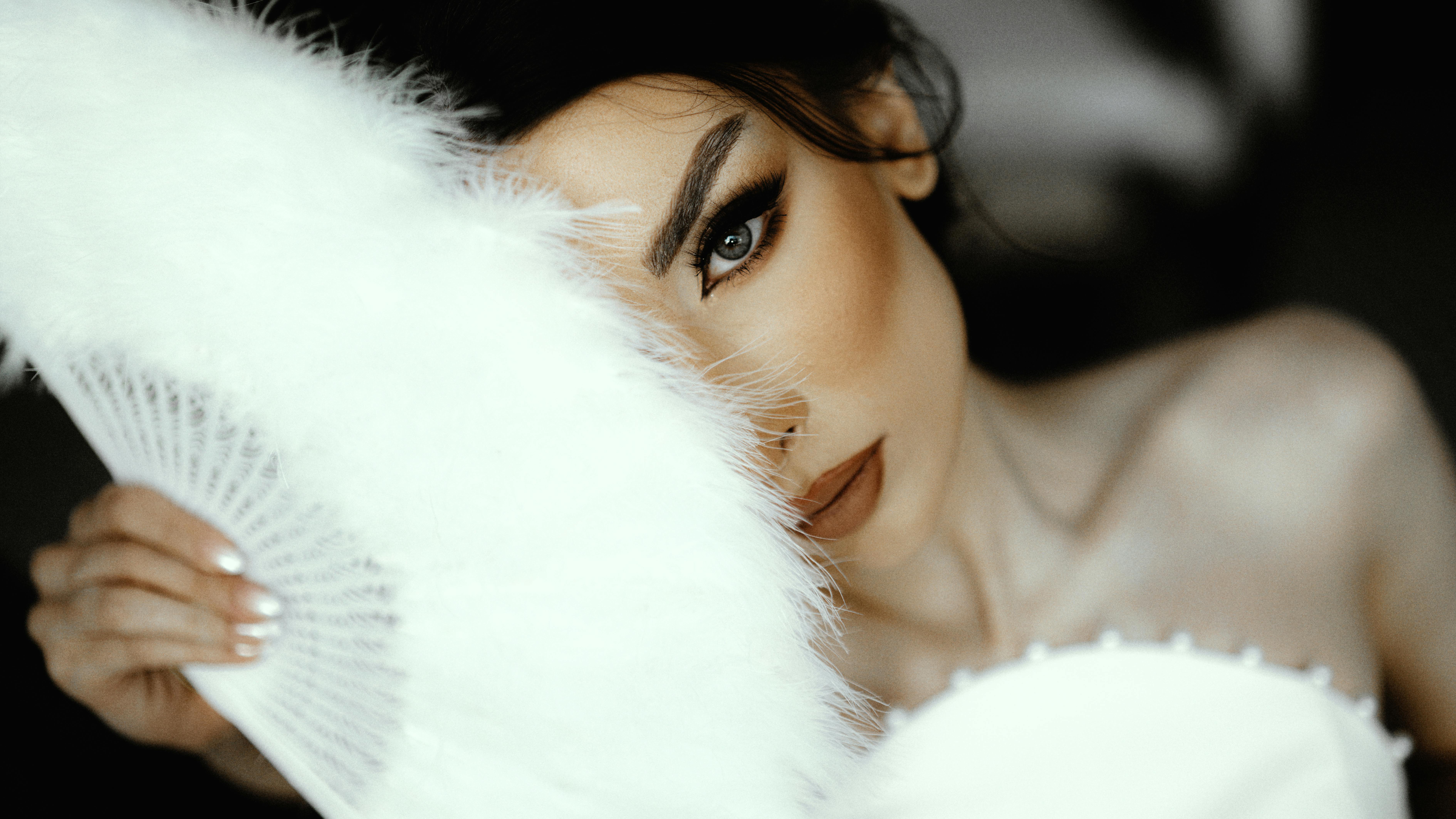 Close-up of a bride's face partially hidden by a feather fan, exuding elegance and mystery.