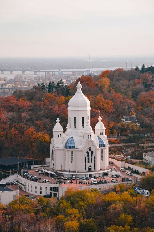 Free Aerial view of St. Nicholas Church in Kyiv, surrounded by autumn foliage, with the cityscape in the background. Stock Photo