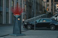 Red geometric sculpture and black car in urban Kyiv setting, showcasing modern art against city backdrop.