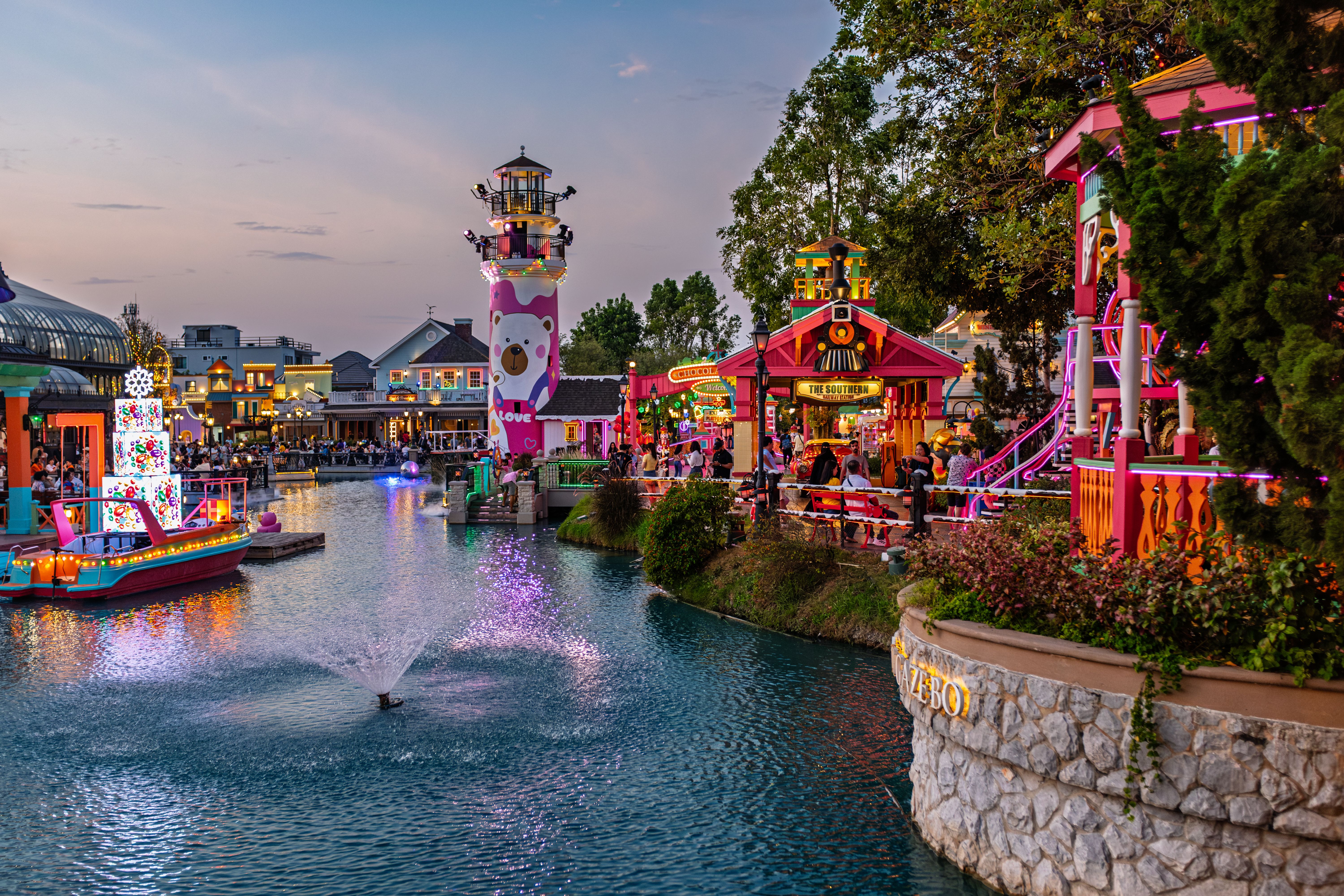 Vibrant amusement park canal scene at twilight with colorful lights and attractions.