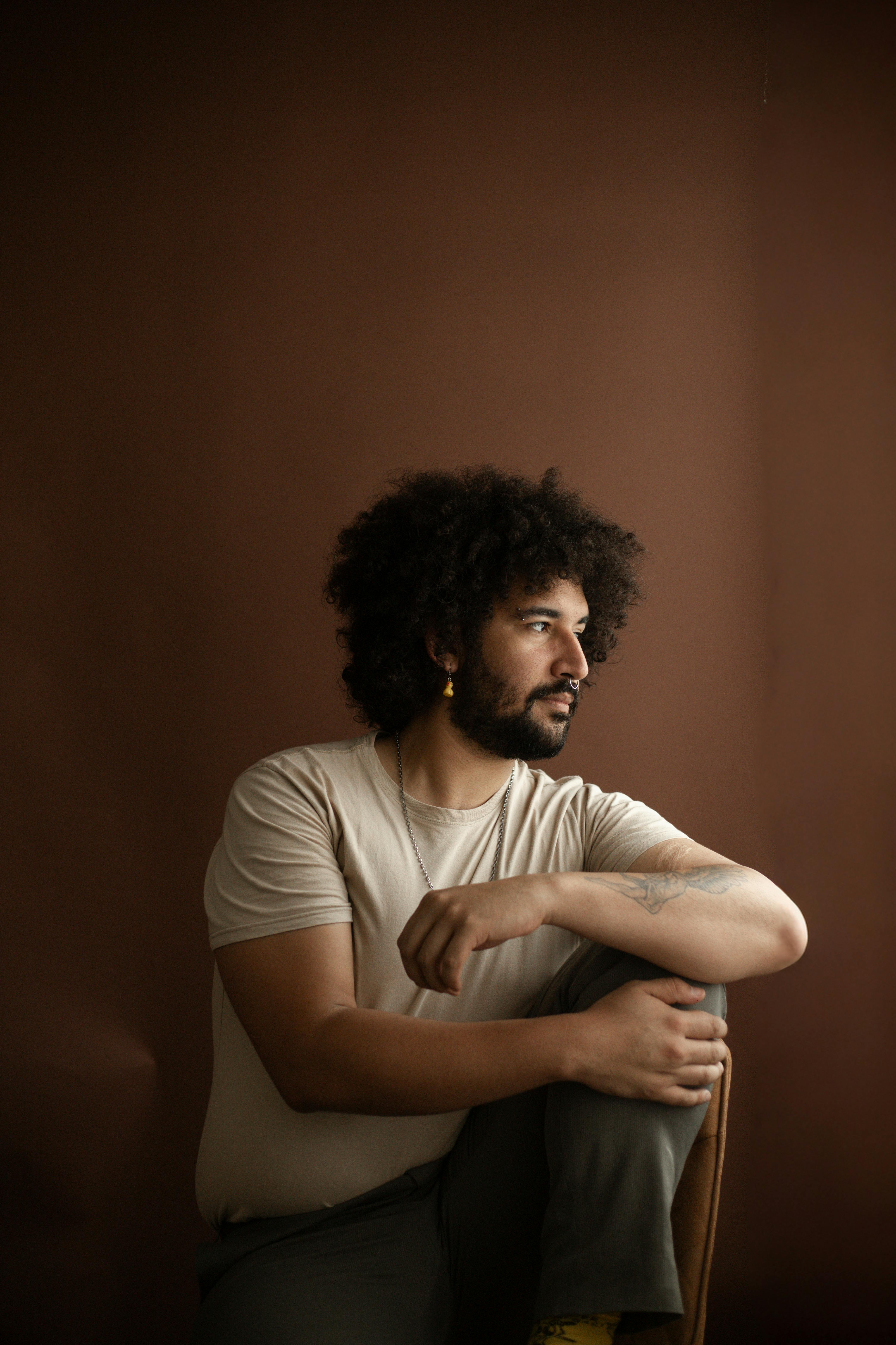 Artistic portrait of a man sitting thoughtfully against a brown backdrop.