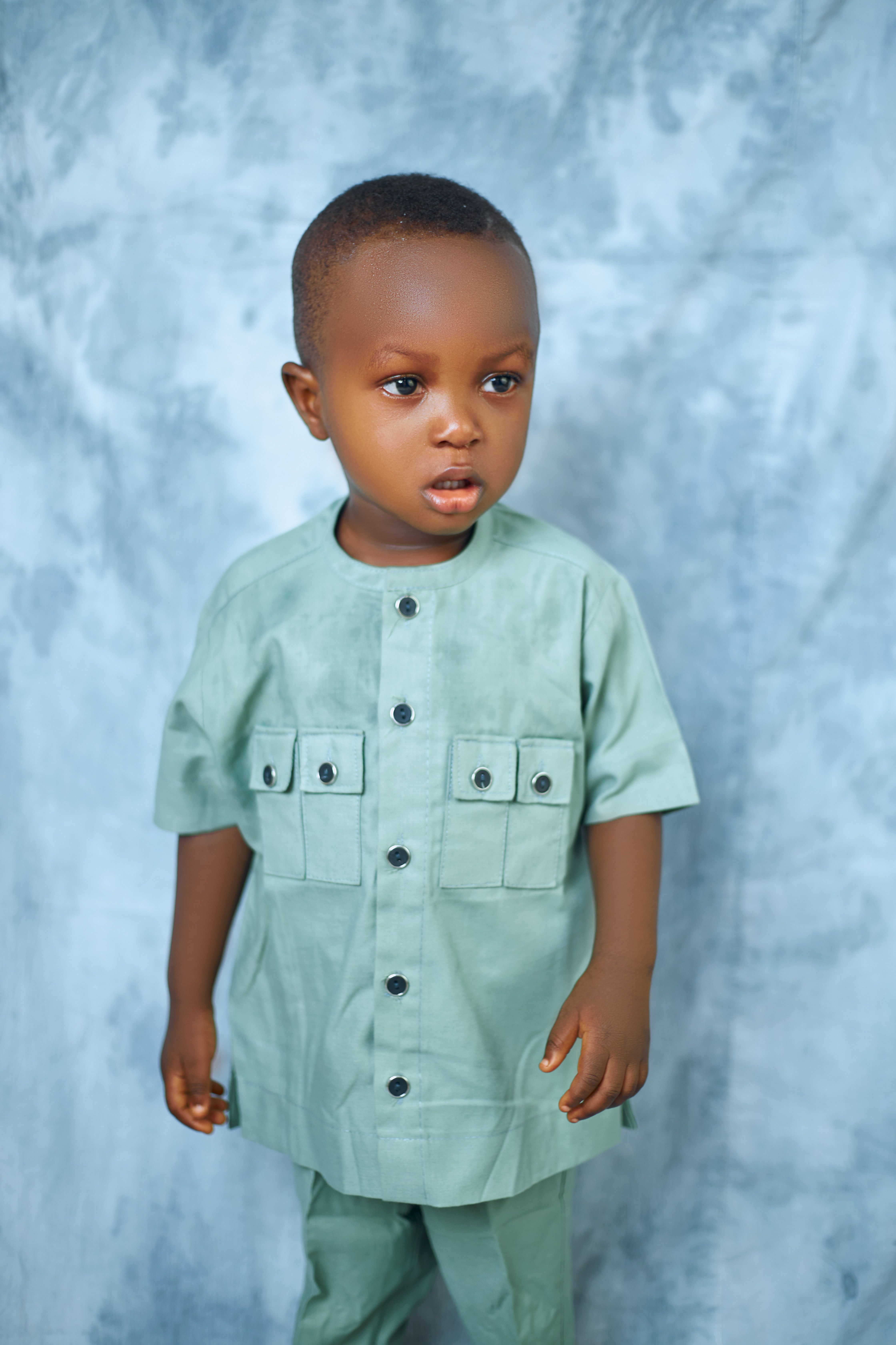 Charming portrait of a young boy in a green traditional outfit with a blue backdrop.