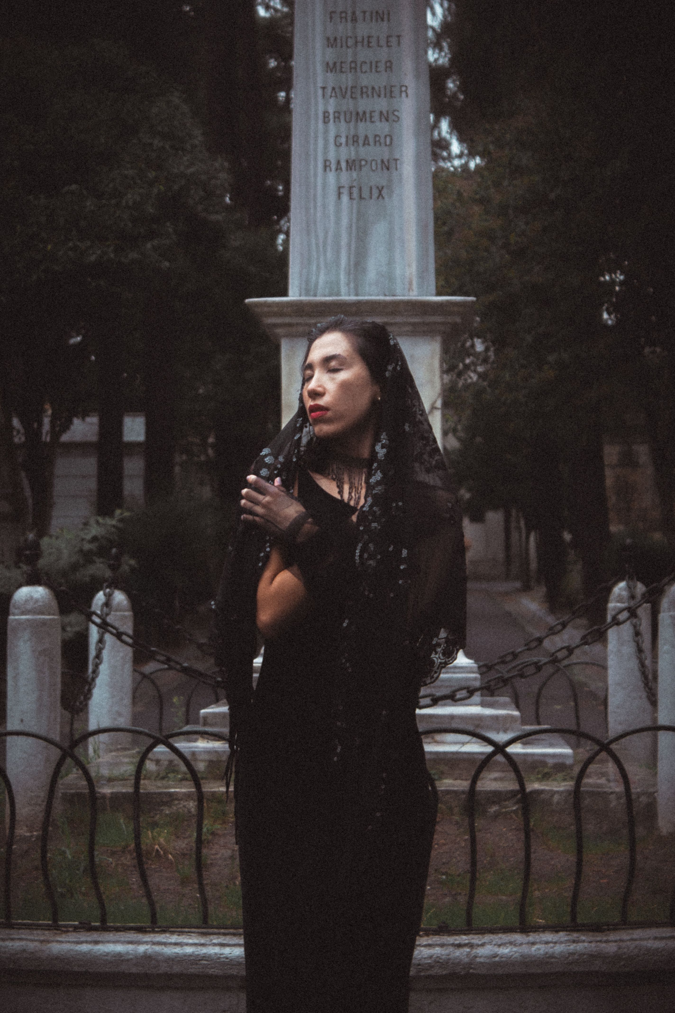 Woman in black veil poses at cemetery, creating a mysterious, gothic vibe.