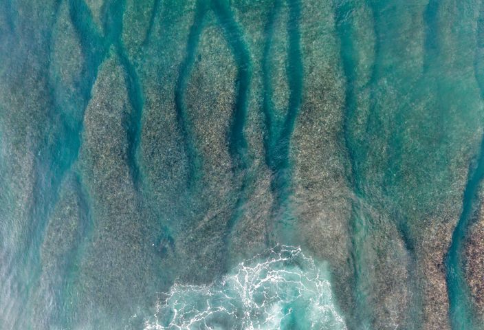 Explore the striking beauty of Bali's coral reefs and turquoise ocean waves from an aerial perspective.