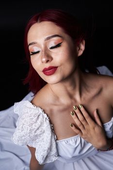 Graceful woman in white dress posing with eyes closed and red lips.
