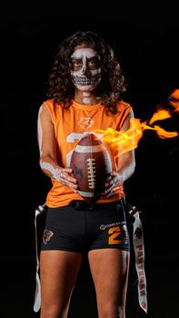 Female football player in Halloween costume with skull makeup holding flaming football.