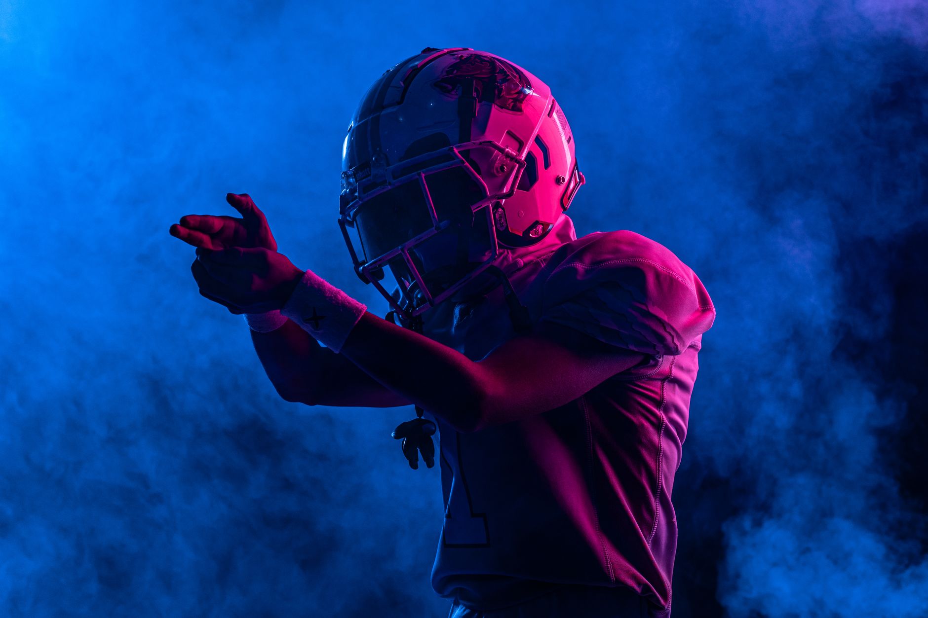 Silhouette of a football player in gear and helmet amidst colorful smoke, dramatic lighting.