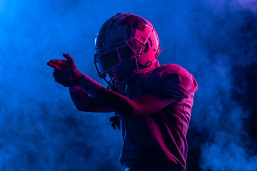 Silhouette of a football player in gear and helmet amidst colorful smoke, dramatic lighting.