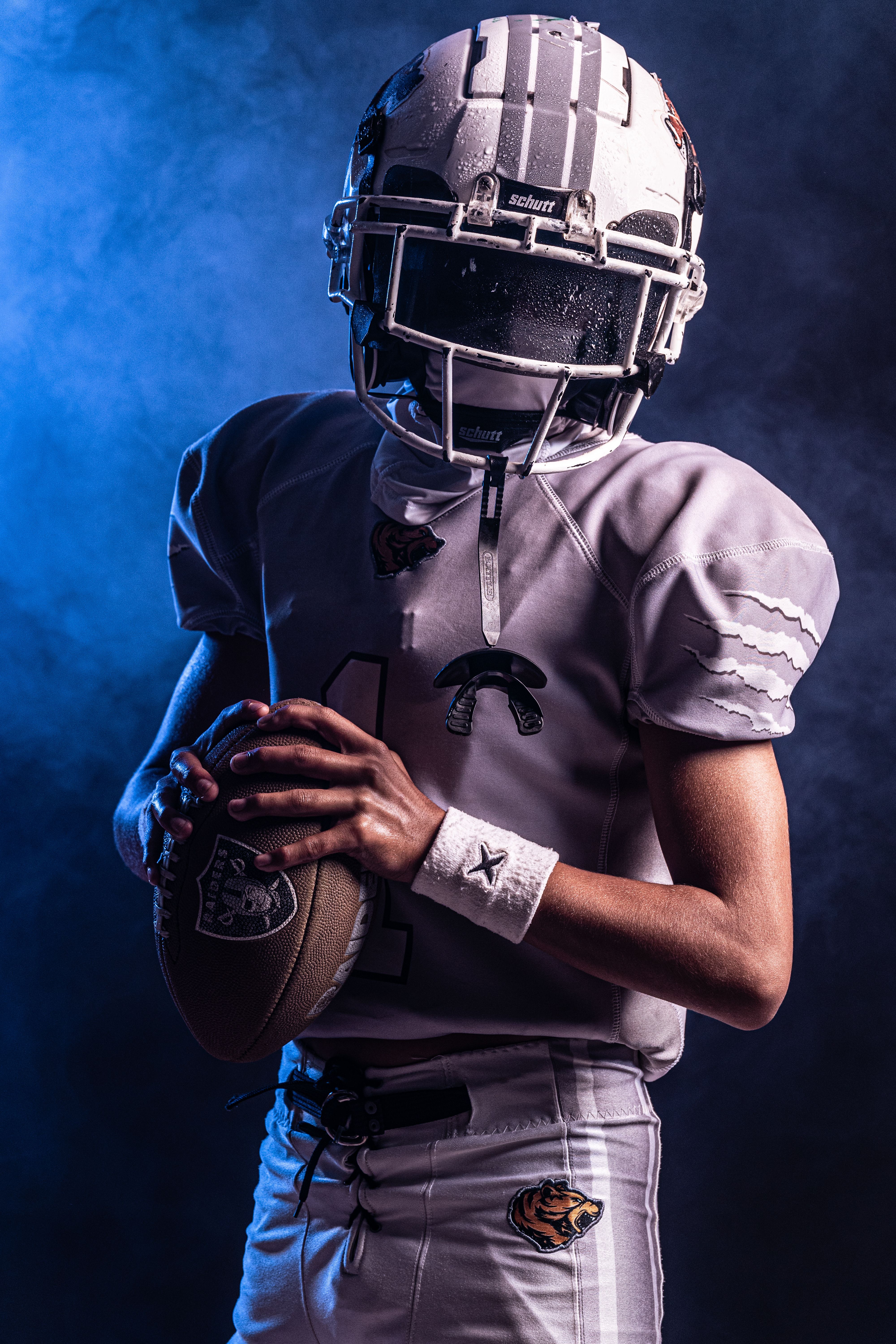 Teen football player in full gear holding a football, with dramatic lighting.