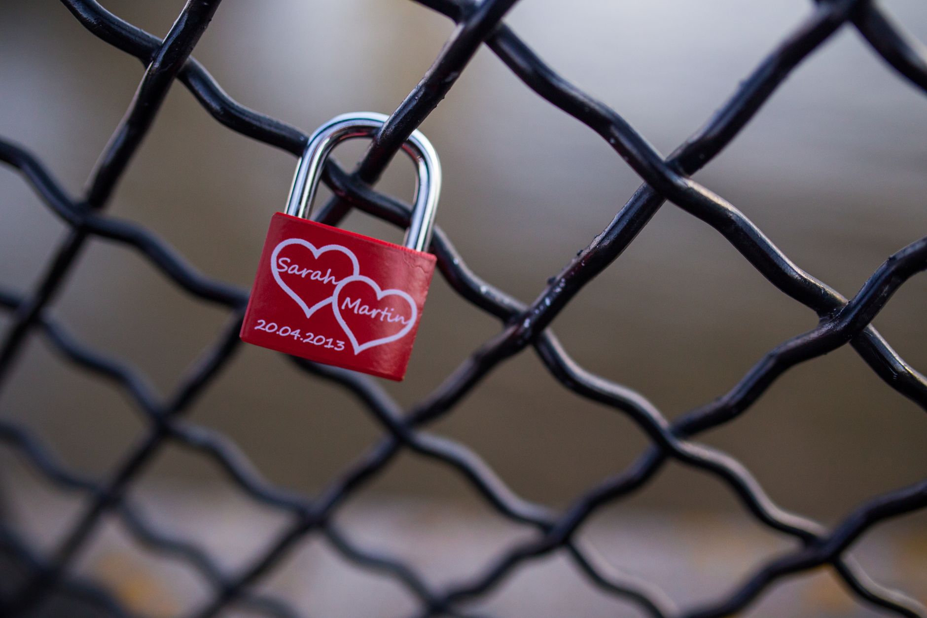 A red love padlock with names on a chain link fence, symbolizing eternal love.