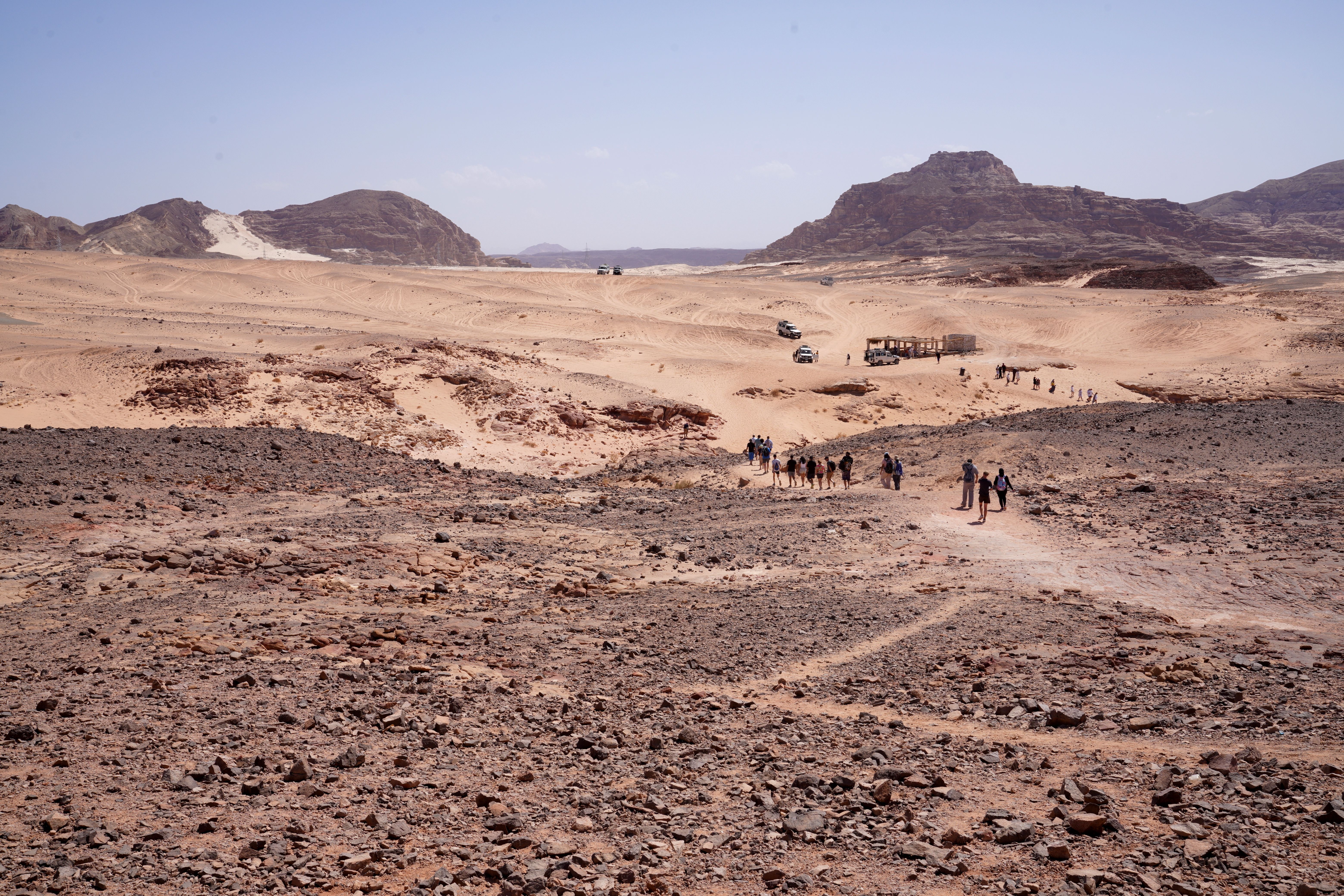 A group of explorers walking through the rugged terrain of the Egyptian desert under clear blue skies.