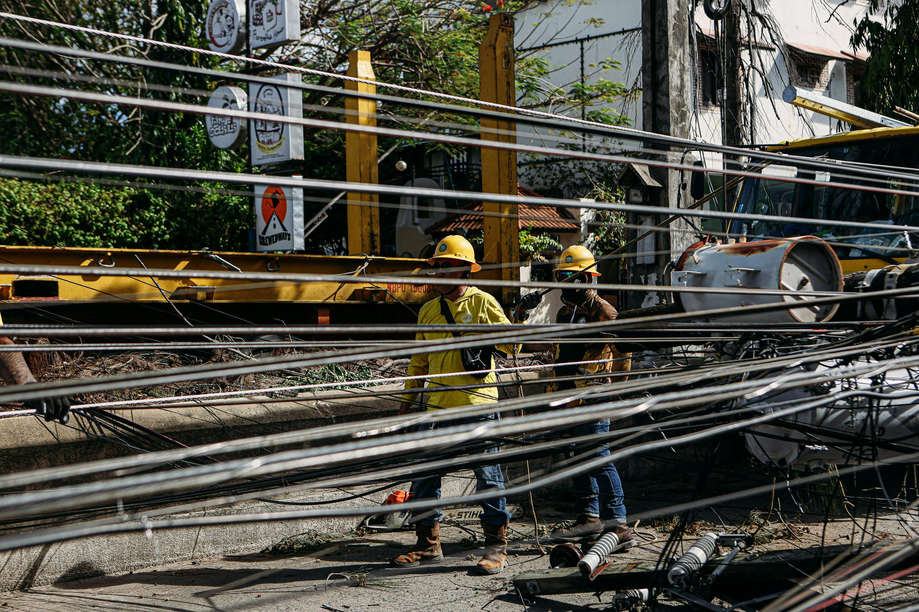 Utility workers in hard hats repair fallen power lines on a sunny day, ensuring electrical safety.