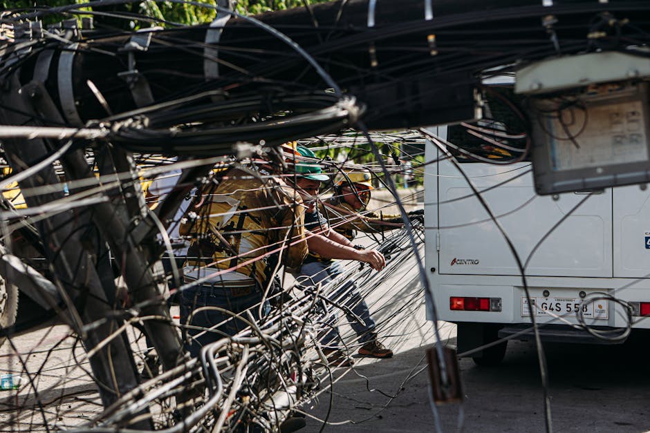 Workers managing tangled power lines by a street setup near a vehicle, highlighting infrastructure challenges.