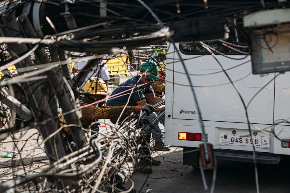 Technicians working on tangled overhead wires next to a vehicle on a sunny day.