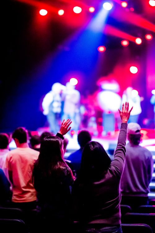 Free Energetic concert scene with audience members raising their hands under vibrant lighting. Stock Photo