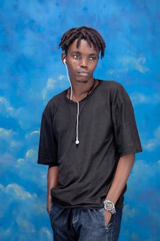 Portrait of a stylish young man wearing earphones against a vibrant blue sky background.