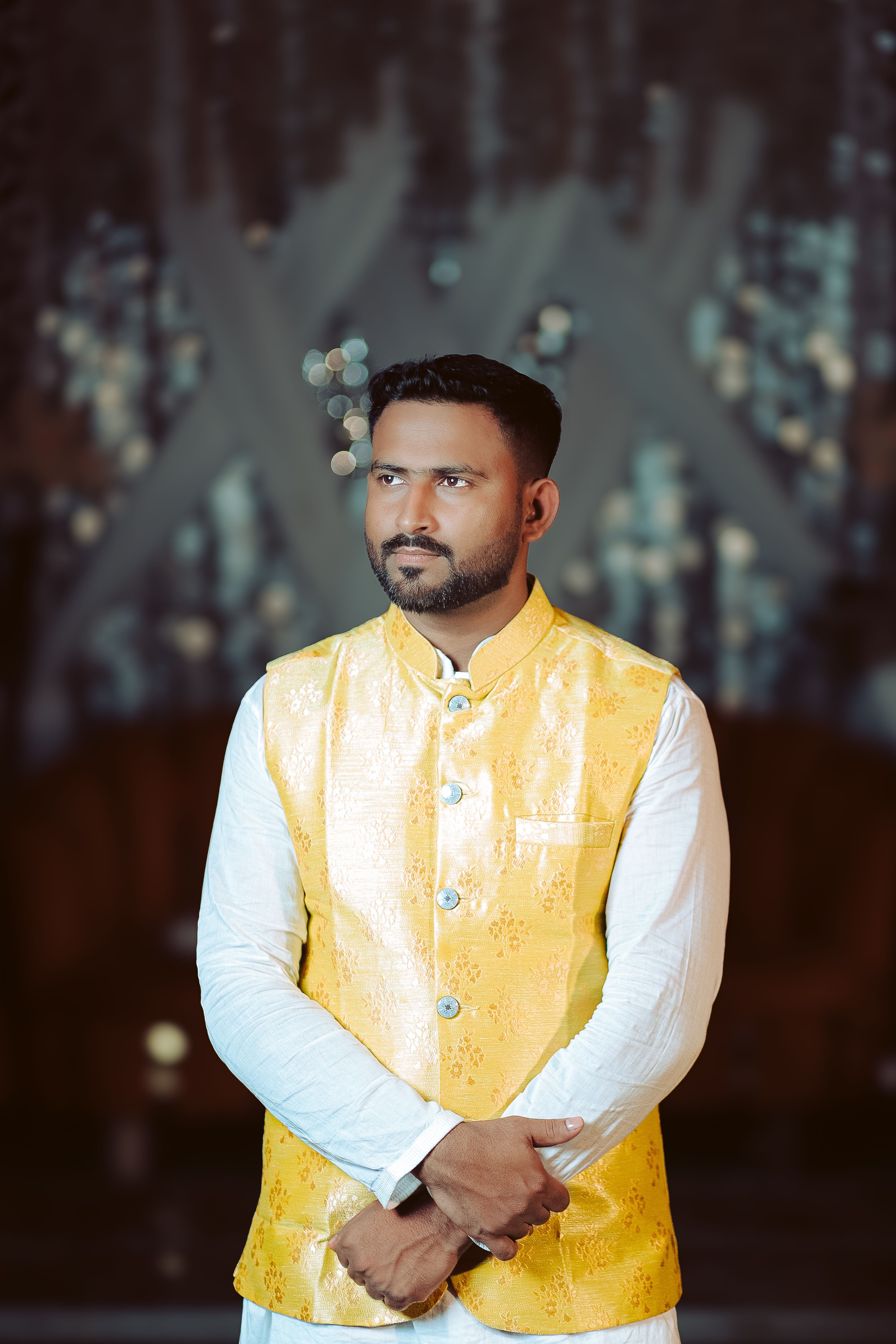 Portrait of a man in yellow traditional attire posing indoors with a blurred background.