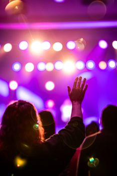 Audience member raises hand in a colorful, vibrant concert atmosphere with stage lights.