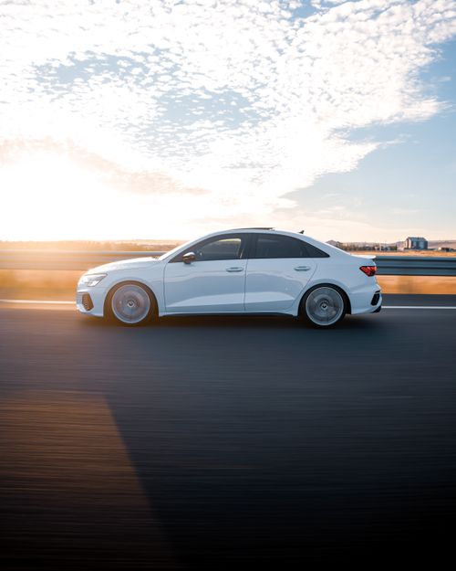 Free A dynamic shot of a white sedan driving on a highway at sunrise, showcasing speed and elegance. Stock Photo