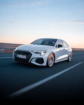 A modern white car speeds along a highway during sunset in Ankara, Türkiye.
