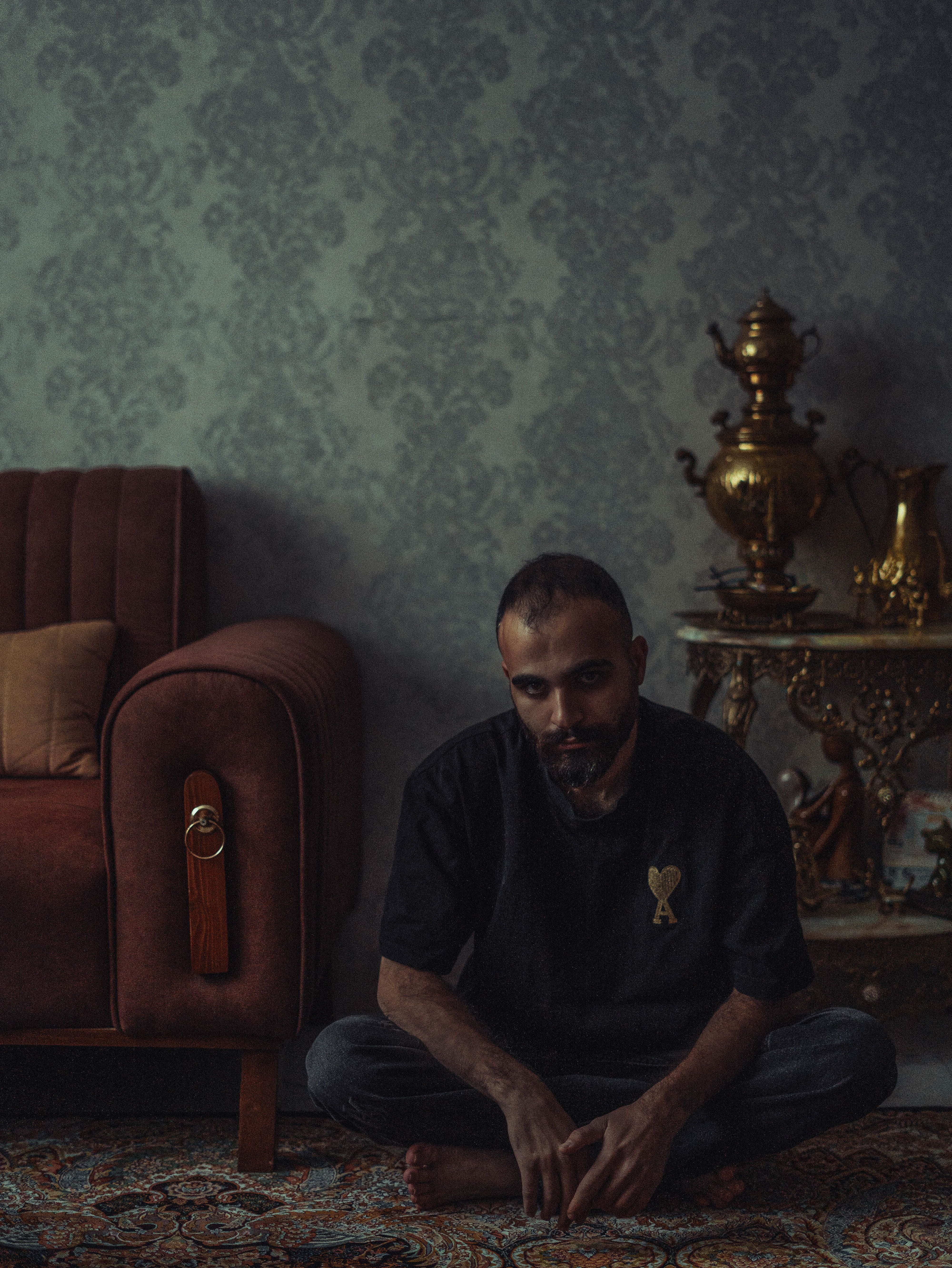 A thoughtful man sitting on a carpeted floor in a vintage-styled living room.