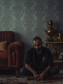 A thoughtful man sitting on a carpeted floor in a vintage-styled living room.. thoughtful, sitting, carpeted