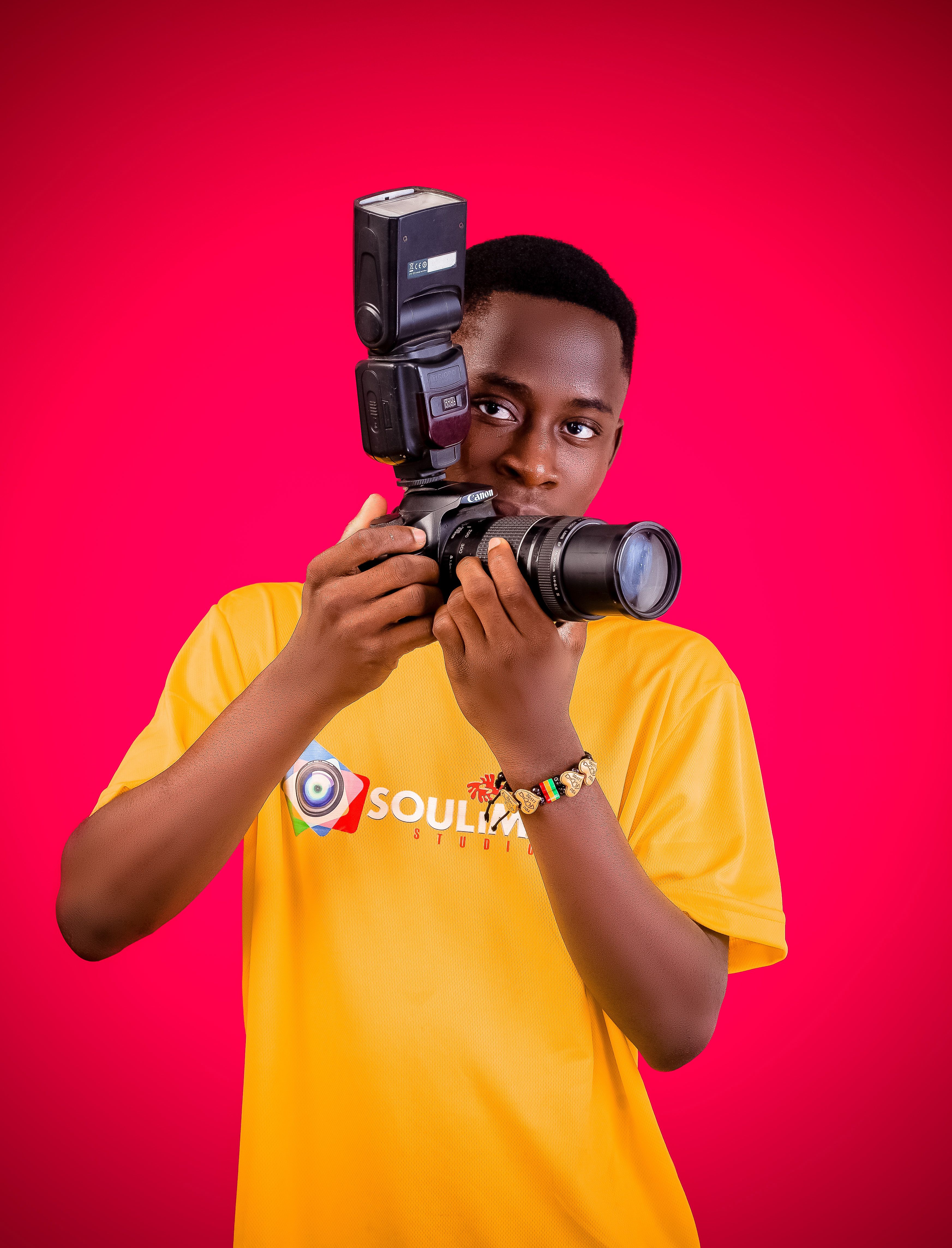 Portrait of a young man with a DSLR camera against a pink background.