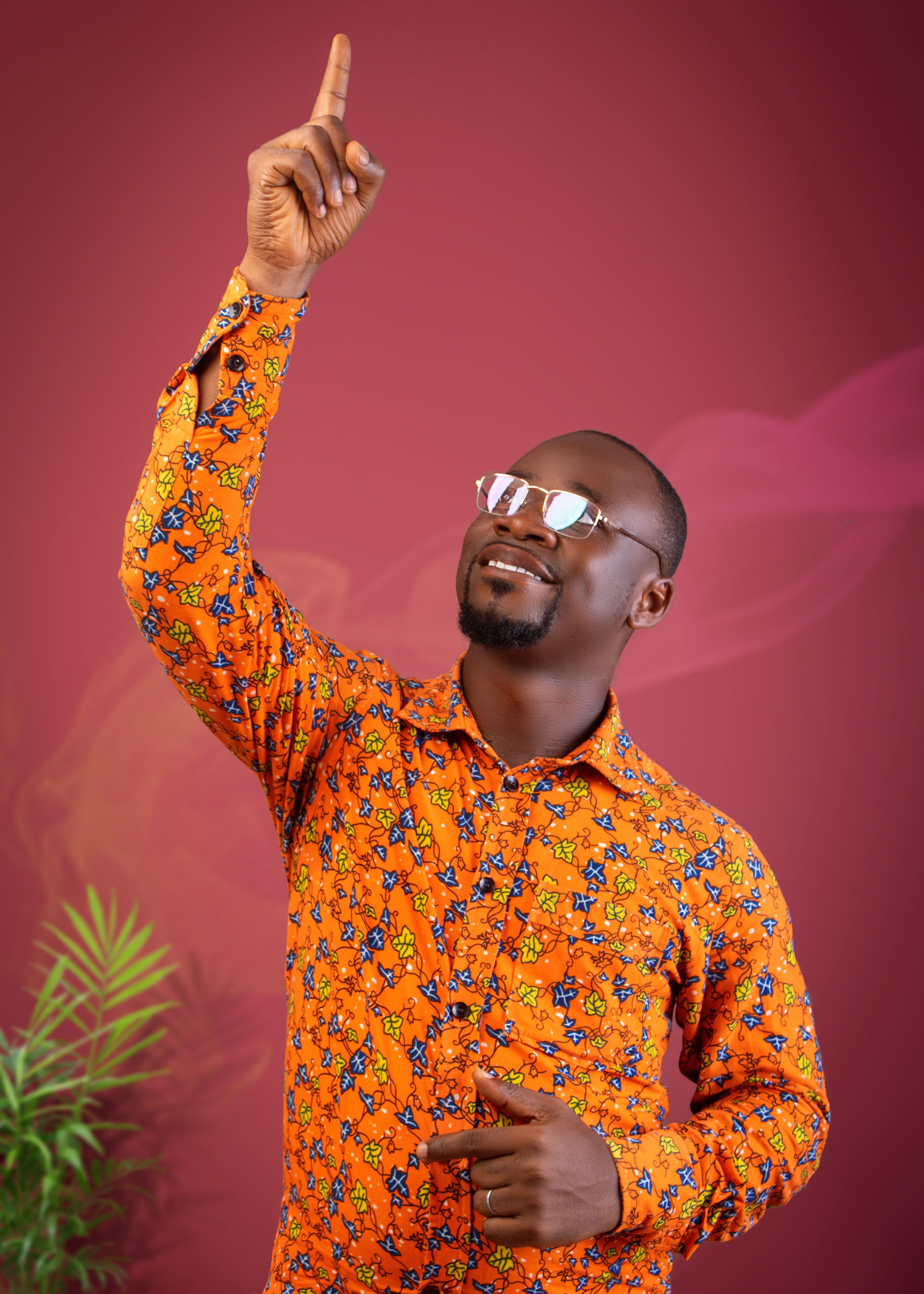 Smiling man in vibrant shirt points upward against a colorful background.