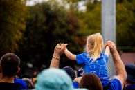 Child on shoulders in a crowd at a sunny outdoor event.