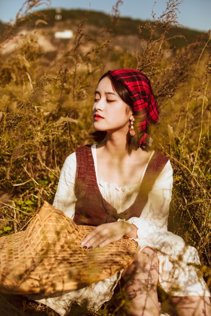 A woman in a vintage outfit enjoys the autumn sun in a field of tall grass.