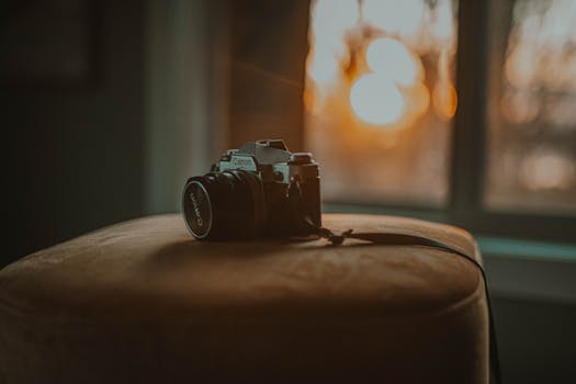 A vintage Canon camera sits on a chair by the window bathed in warm sunset glow.