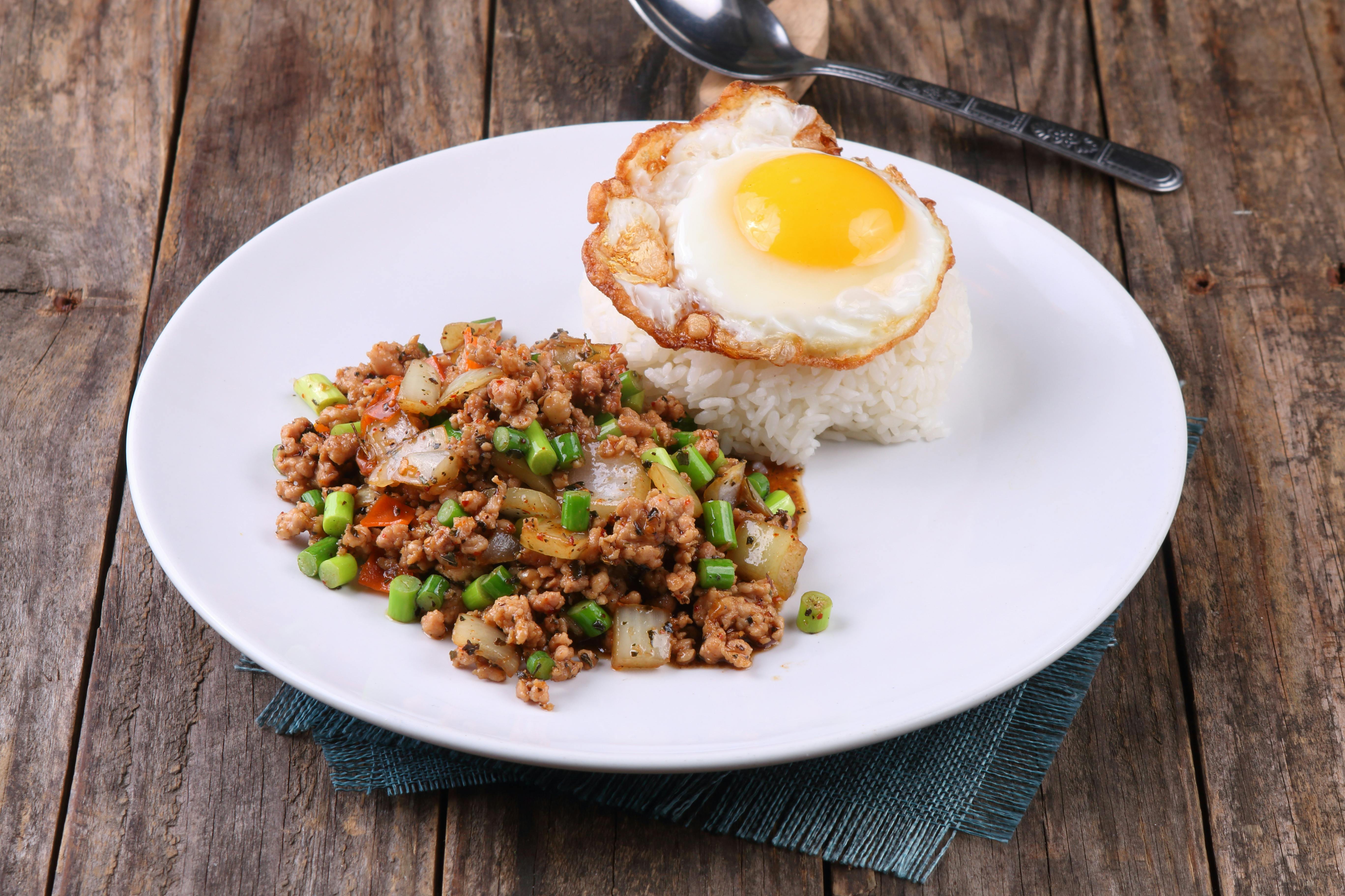 Delicious stir-fried pork with rice and sunny-side up egg on a wooden table setting.