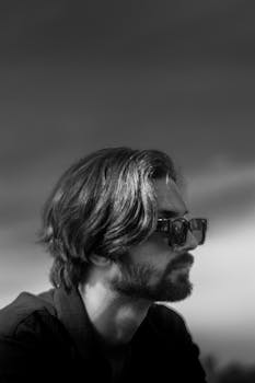 Black and white profile portrait of a stylish bearded man in sunglasses outdoors.